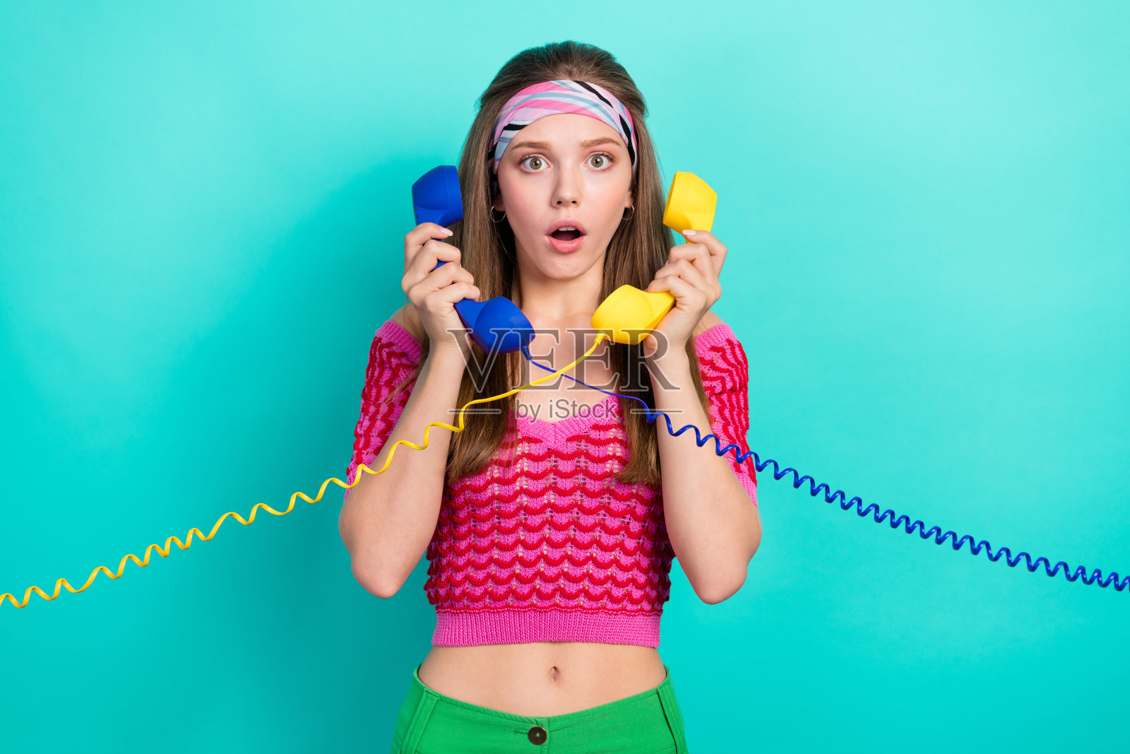 惊讶的女孩,直发,粉色上衣,头带,正在使用座机,背景为青绿色。照片摄影图片