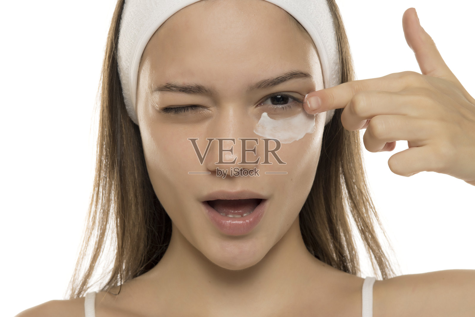 美丽。年轻微笑的女性在白色背景下涂抹眼部化妆霜。照片摄影图片