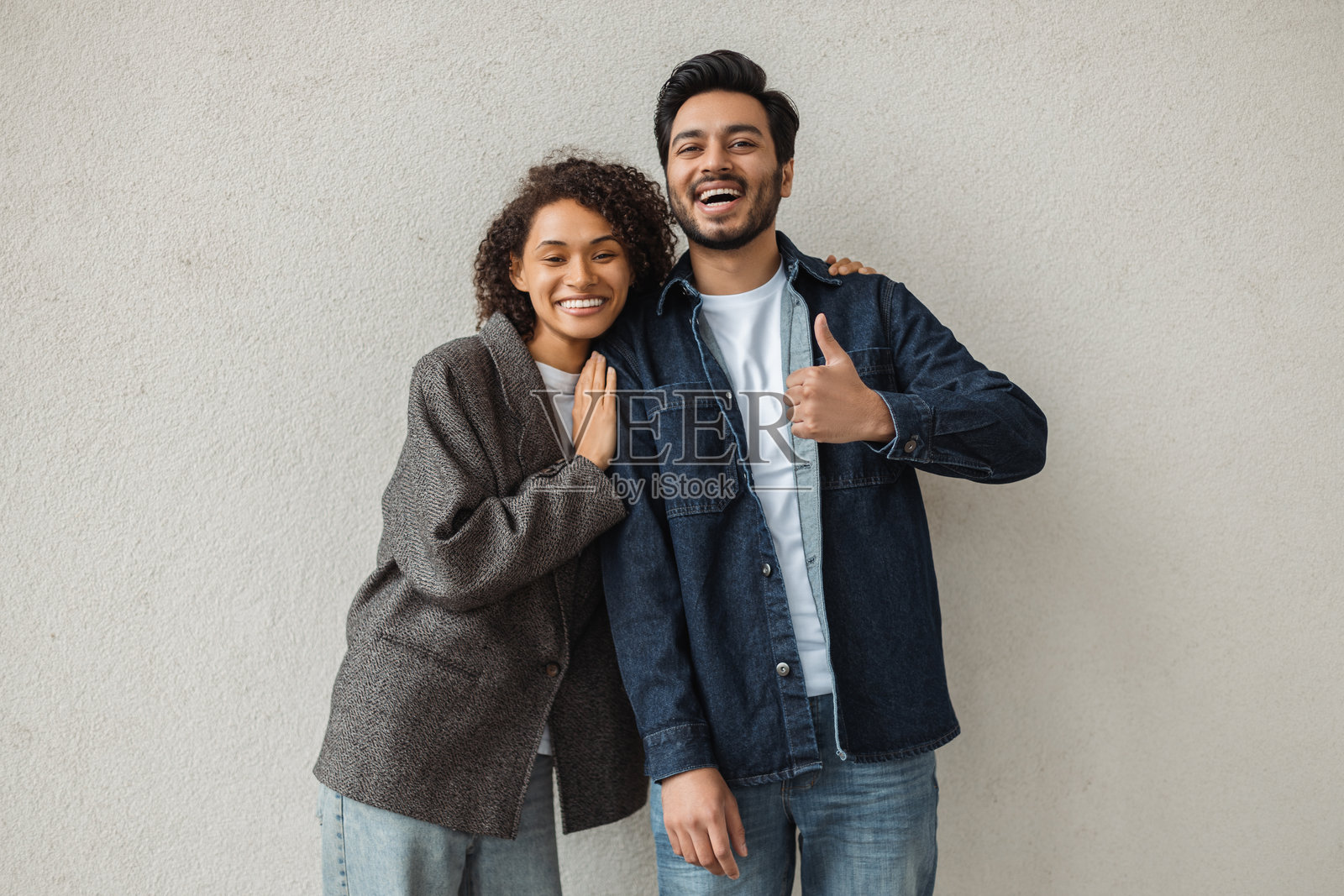 快乐的多种族情侣在灰色墙壁前竖起大拇指微笑照片摄影图片