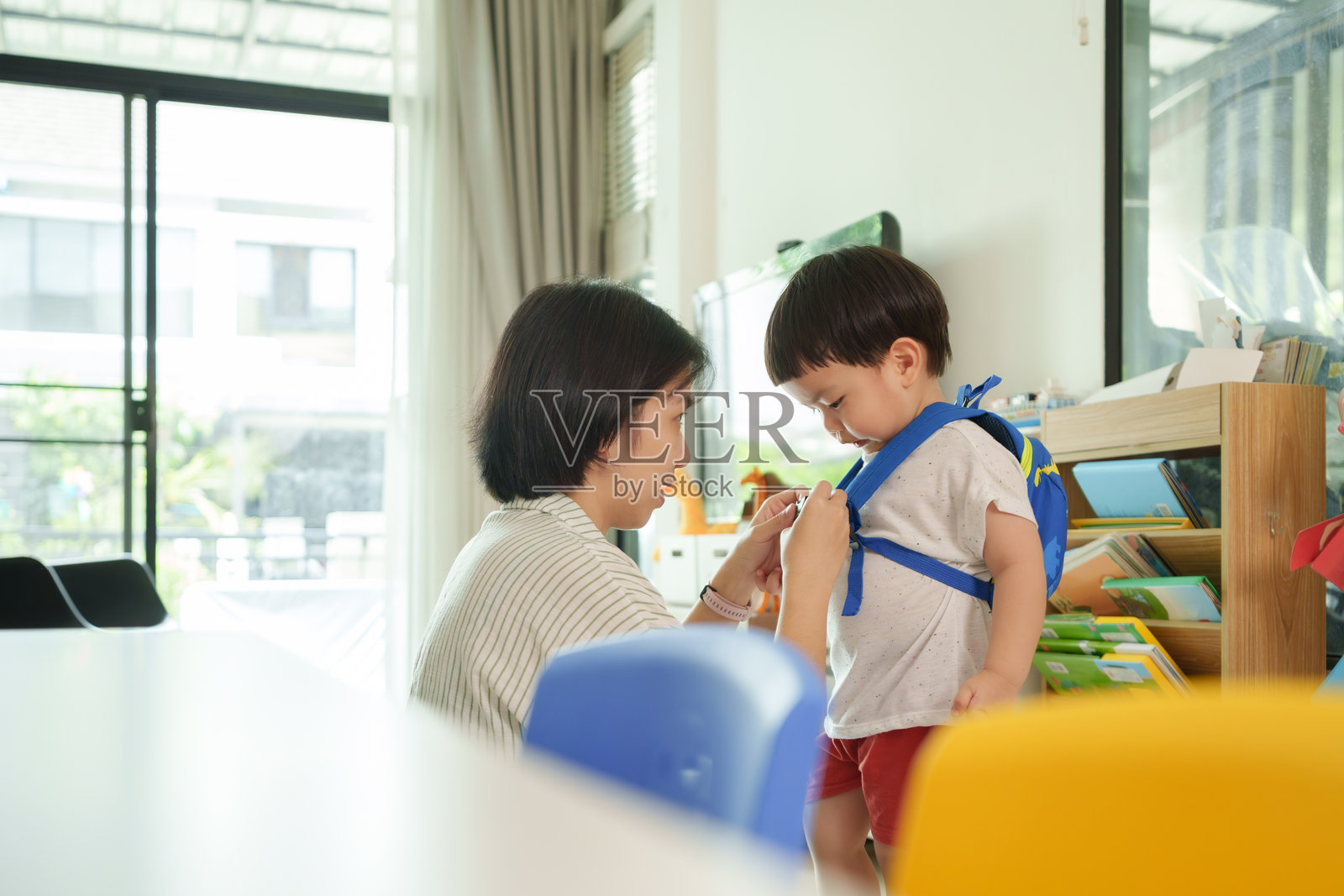 亚洲母亲在家中的客厅为年轻儿子调整背包,准备上学。照片摄影图片
