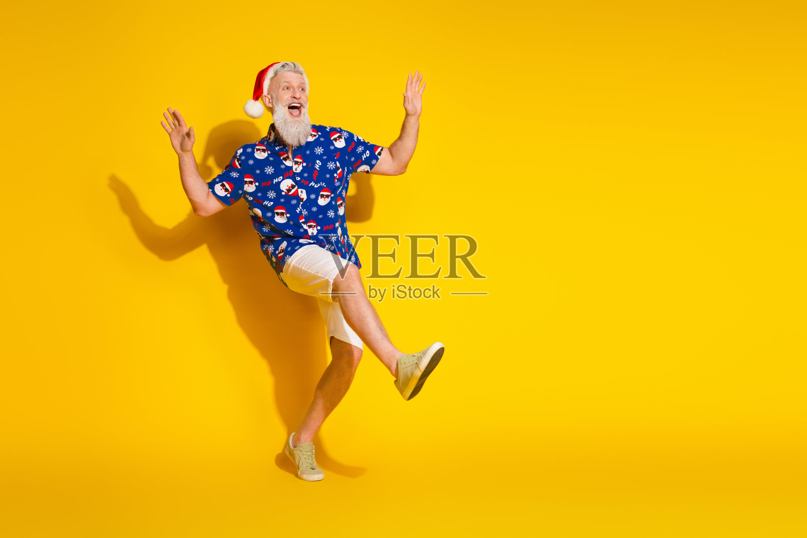 全身肖像的时尚圣诞老人,穿着圣诞图案衬衫,跳舞,背景为黄色,周围空旷。照片摄影图片