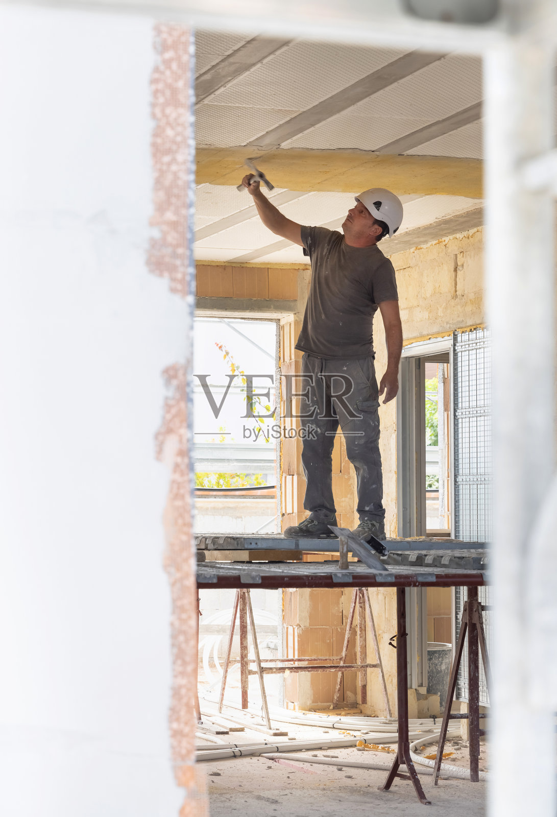 穿着灰色衣服的工匠在房间内的脚手架上进行施工照片摄影图片