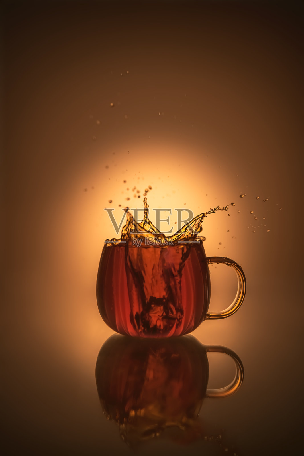 透明杯中茶的创意飞溅摄影,温暖的橙色,留白,静物构图照片摄影图片