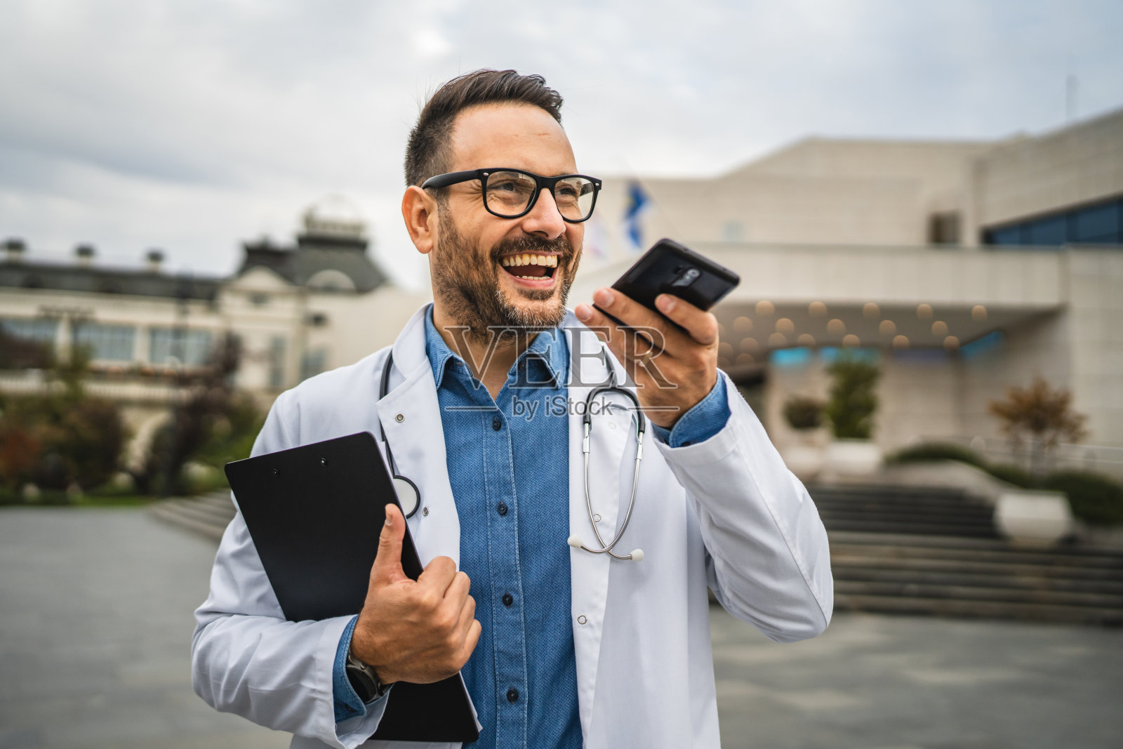医生在户外休息时留下语音留言并拿着夹板。照片摄影图片