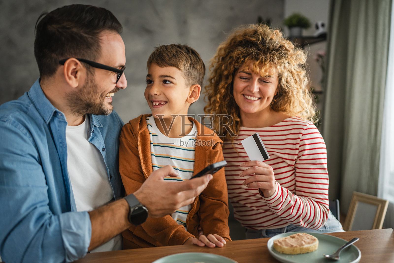 一家三口正在用手机进行在线购物,使用信用卡付款。照片摄影图片