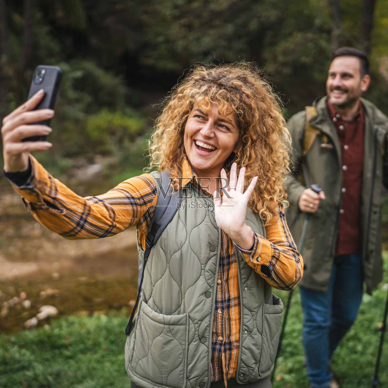 成年女性徒步旅行者在拍摄自拍照,丈夫站在她身后。照片摄影图片