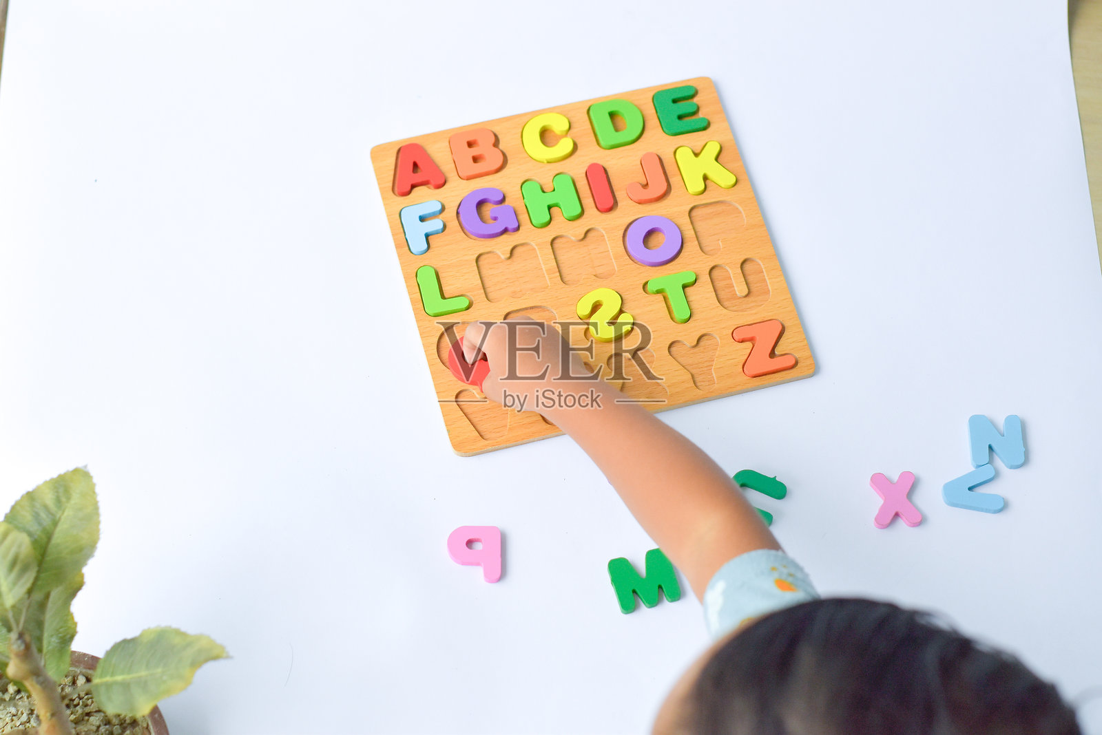 一个3岁的孩子正在通过五彩的木制拼图学习识别字母。照片摄影图片