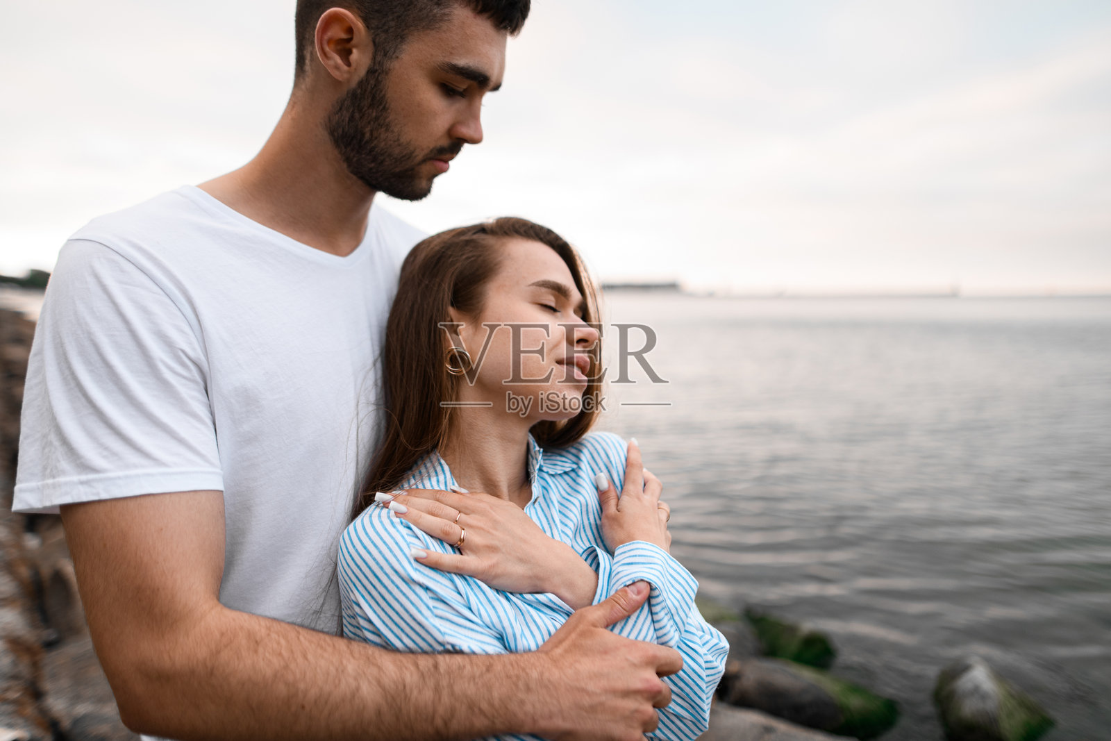 年轻女性在丈夫的怀抱中,丈夫从后面搂着她的肩膀。照片摄影图片