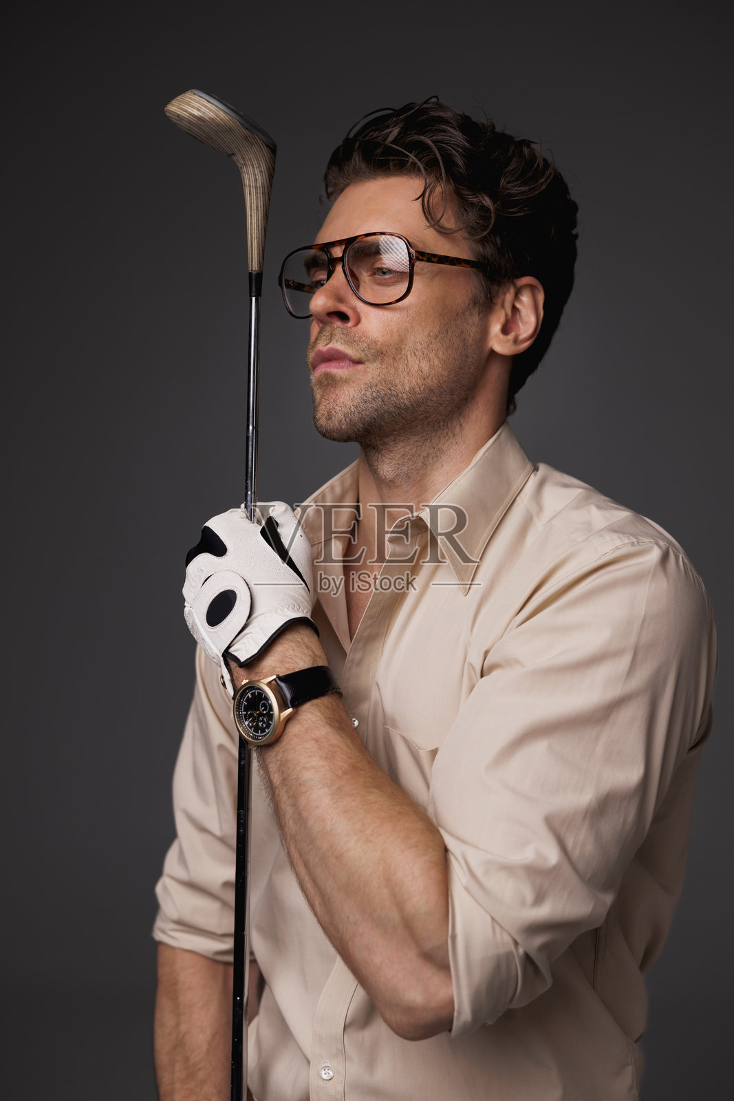 时尚男士戴着眼镜,穿着衬衫,手持高尔夫球杆,背景为灰色。照片摄影图片