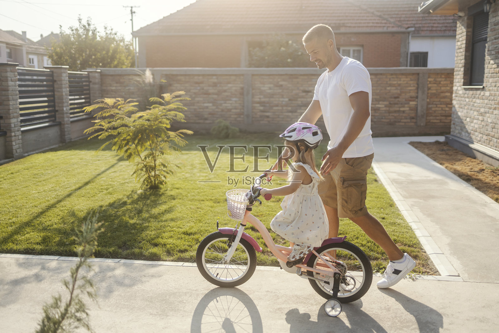 年轻的支持性父亲在后院教他的小女儿骑自行车,享受着快乐的时光。照片摄影图片