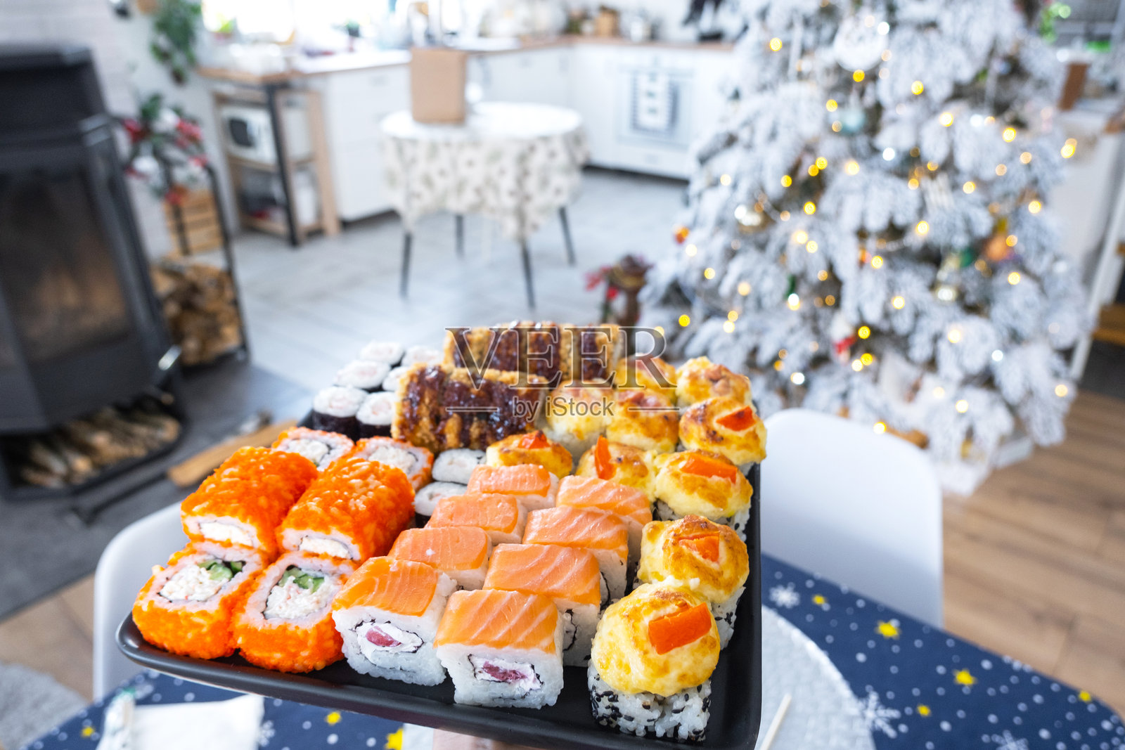 手中拿着寿司和卷的外卖,在装饰有白色圣诞树的节日家居环境中,庆祝圣诞节和新年。节日的美食外卖。照片摄影图片