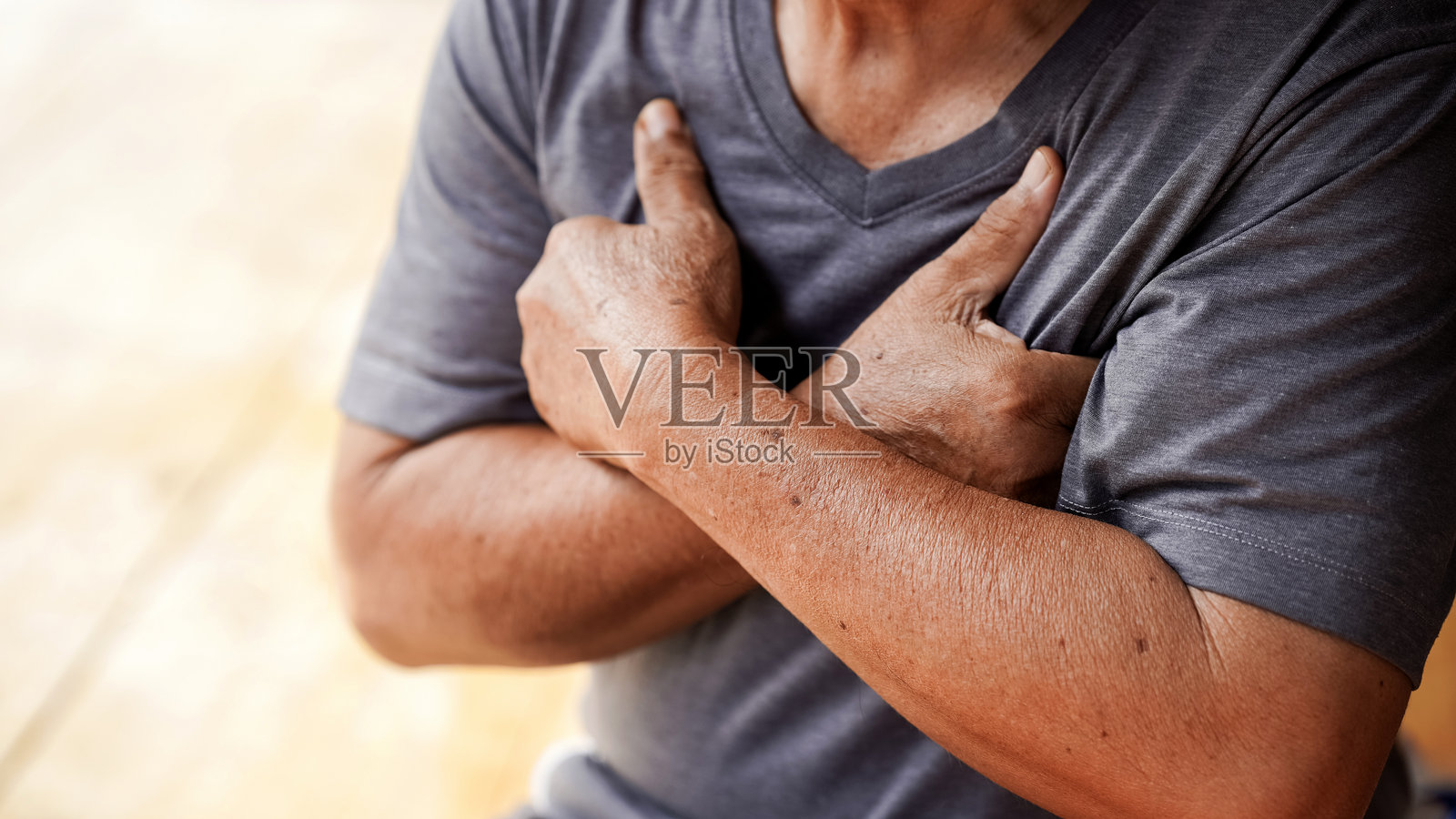 穿着灰色衬衫的老人交叉双臂,流露出深思的表情。重点在于手臂和手,突显皮肤的纹理。照片摄影图片