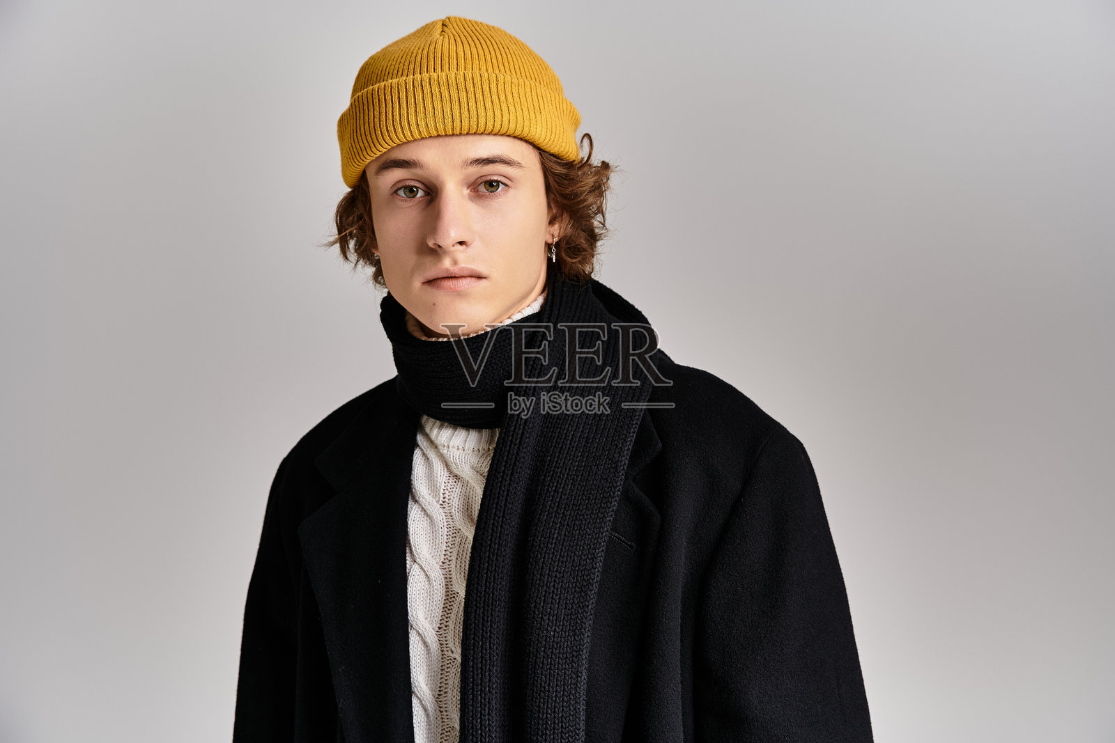 一位穿着黑色外套和黄色毛线帽的年轻人在现代工作室中优雅地摆姿势照片摄影图片