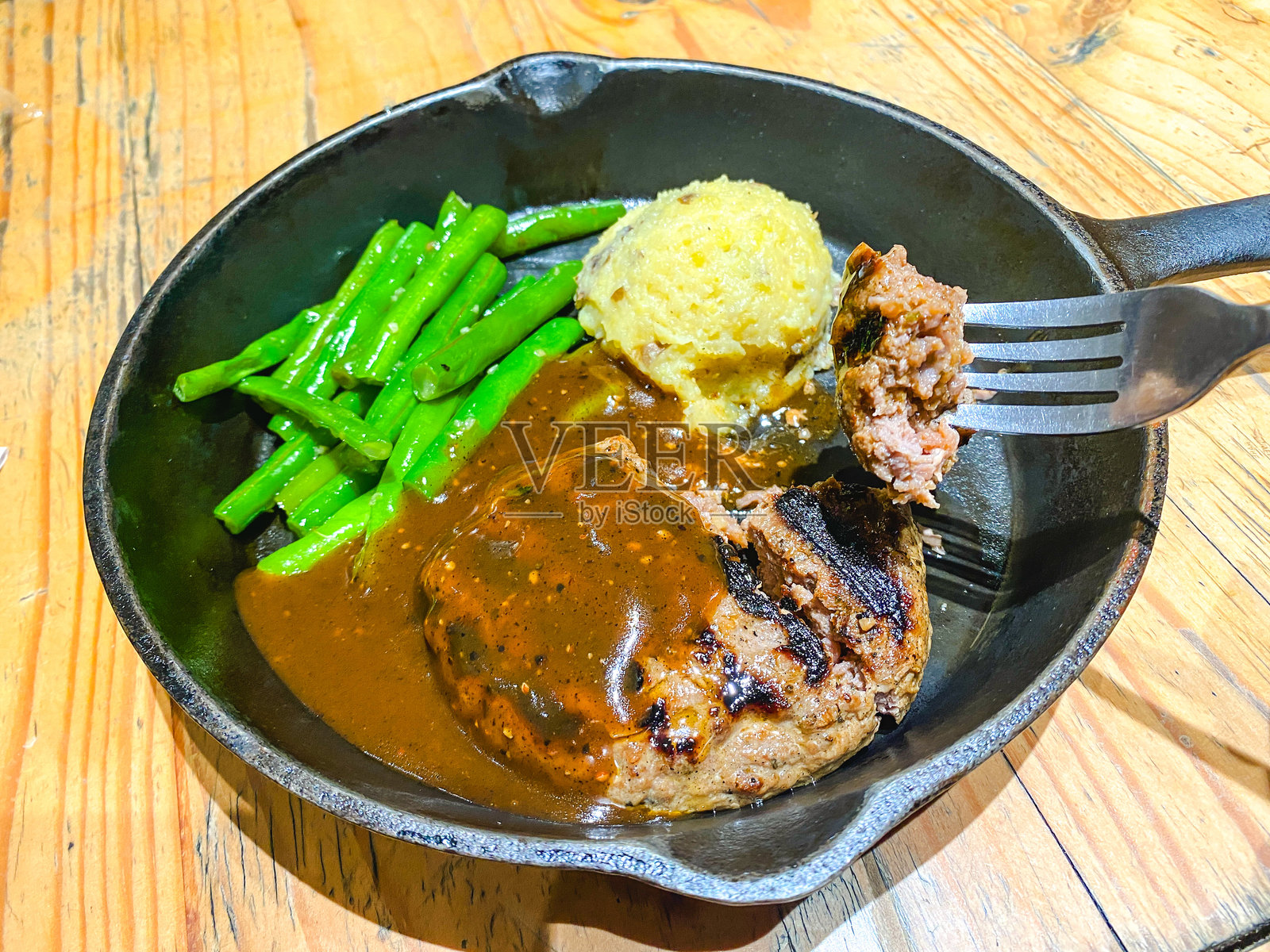 黑色平底锅中的黑胡椒酱汉堡牛排,搭配煮豆和土豆泥一起享用照片摄影图片