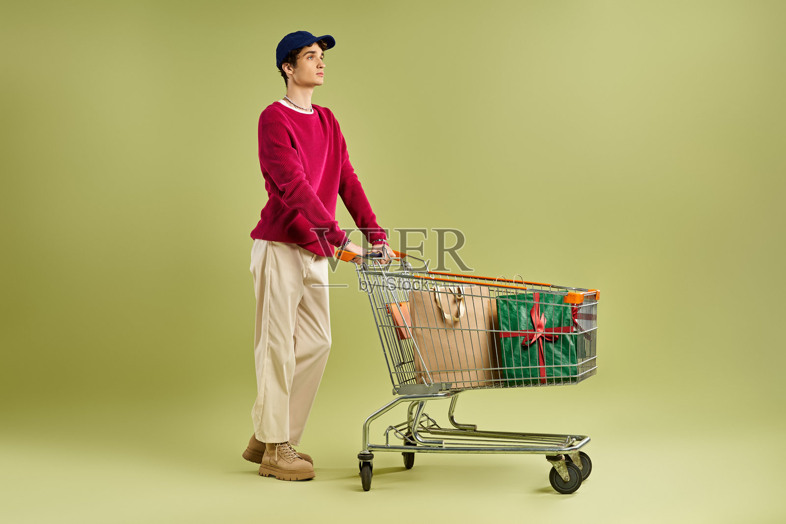 一个快乐的年轻人戴着棒球帽,准备迎接圣诞节,身边有五彩缤纷的礼物。照片摄影图片