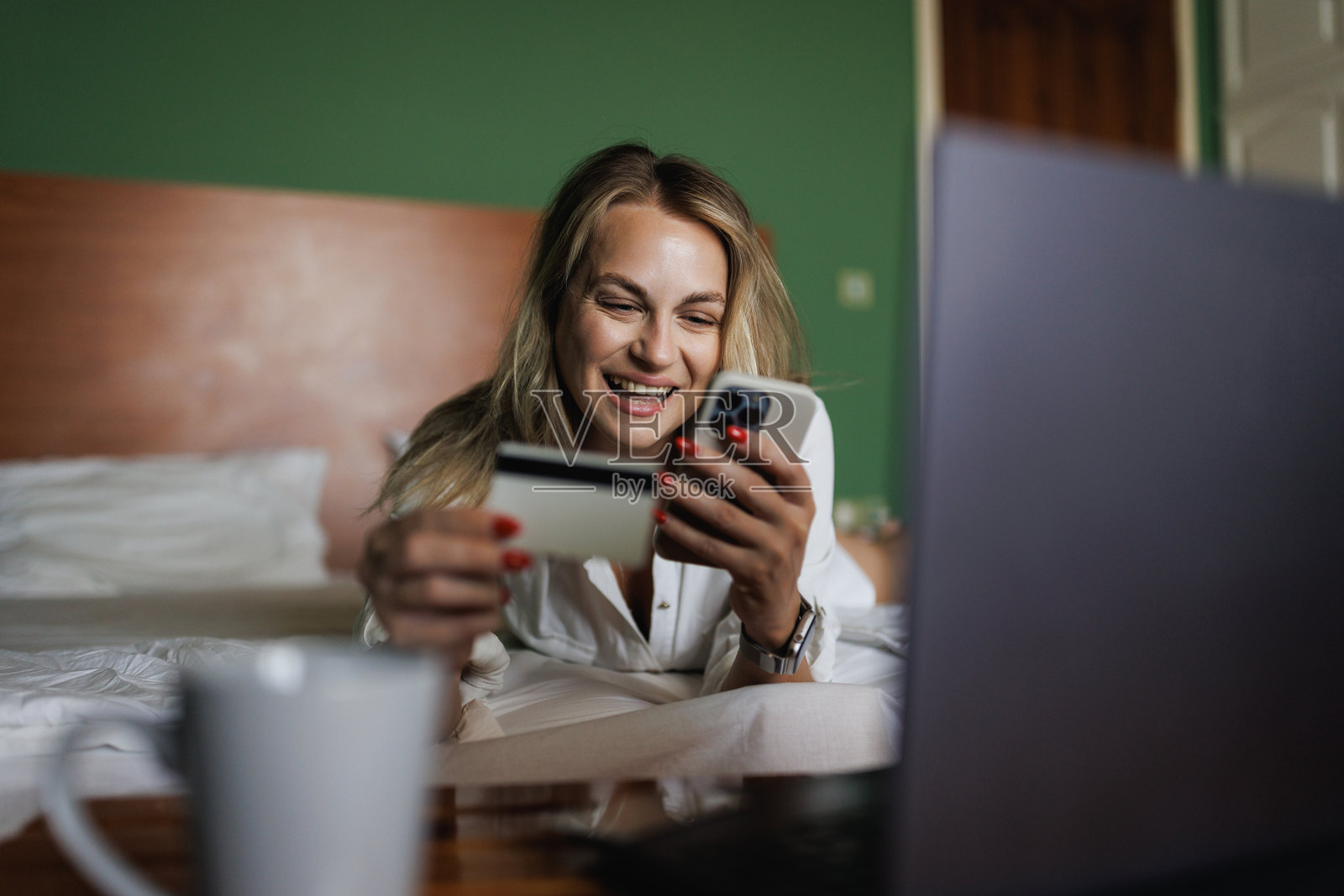 微笑的女性在早晨的床上使用信用卡和智能手机照片摄影图片