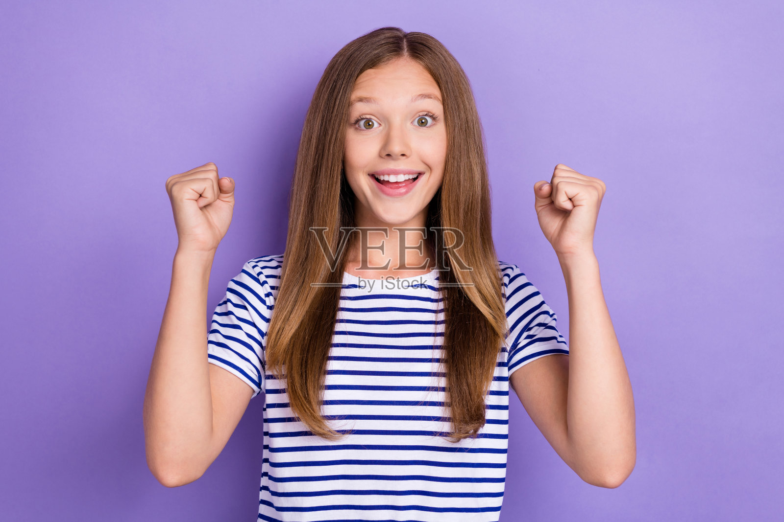 穿着条纹T恤、留着直发的积极乐观女孩,双拳紧握,背景为紫色。照片摄影图片