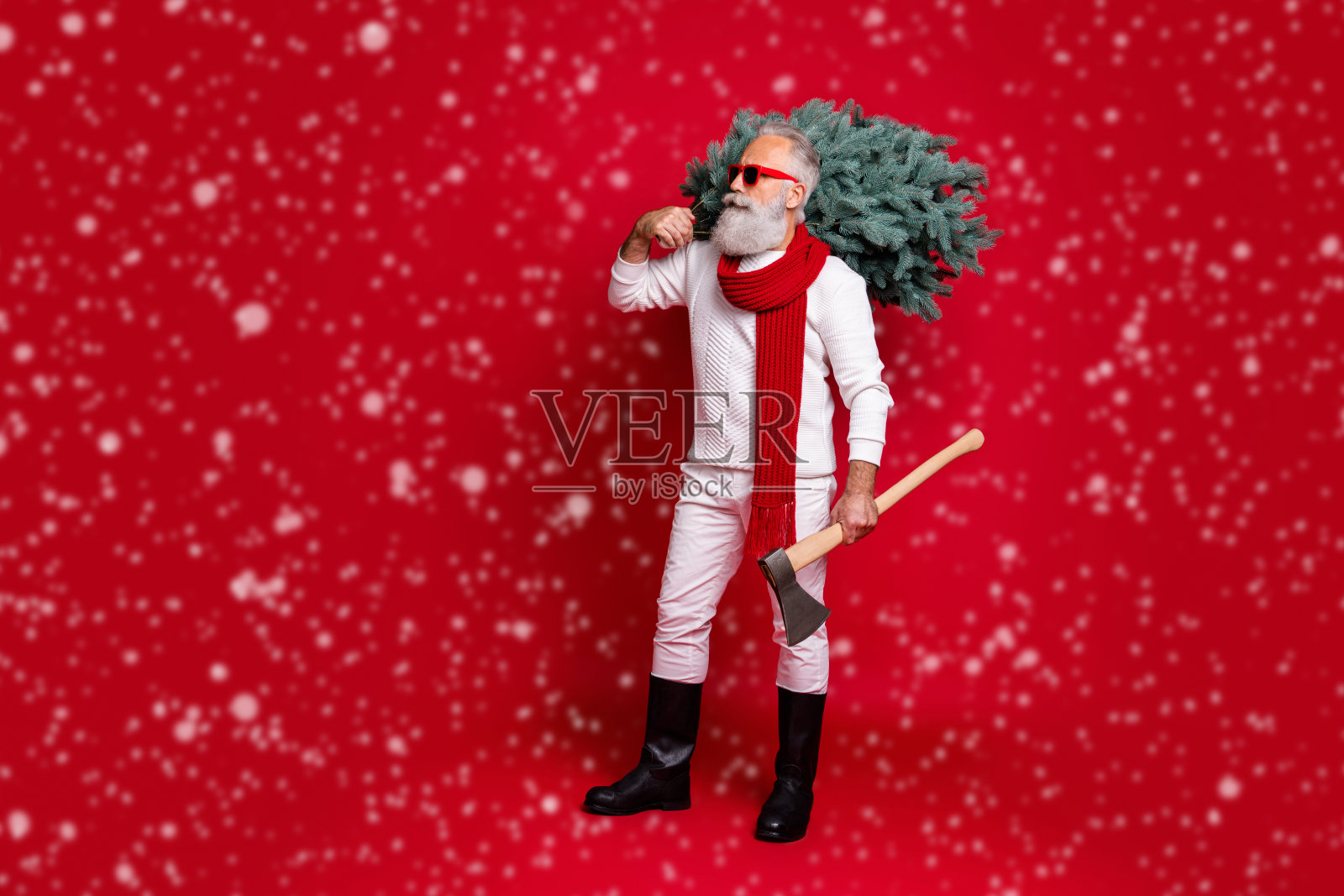 全身长镜头展示了一位英俊、强壮的灰发男士,穿着毛衣、裤子和靴子,手持庆祝用的斧头,背景为明亮鲜艳的红色。照片摄影图片