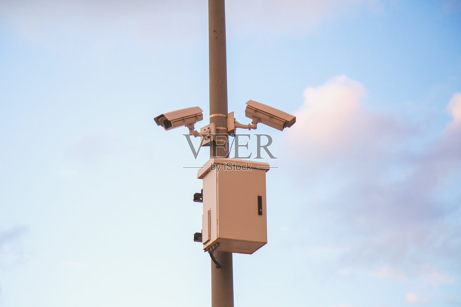 两台街道监控摄像头悬挂在一根杆子上,背景是美丽的日落天空。照片摄影图片