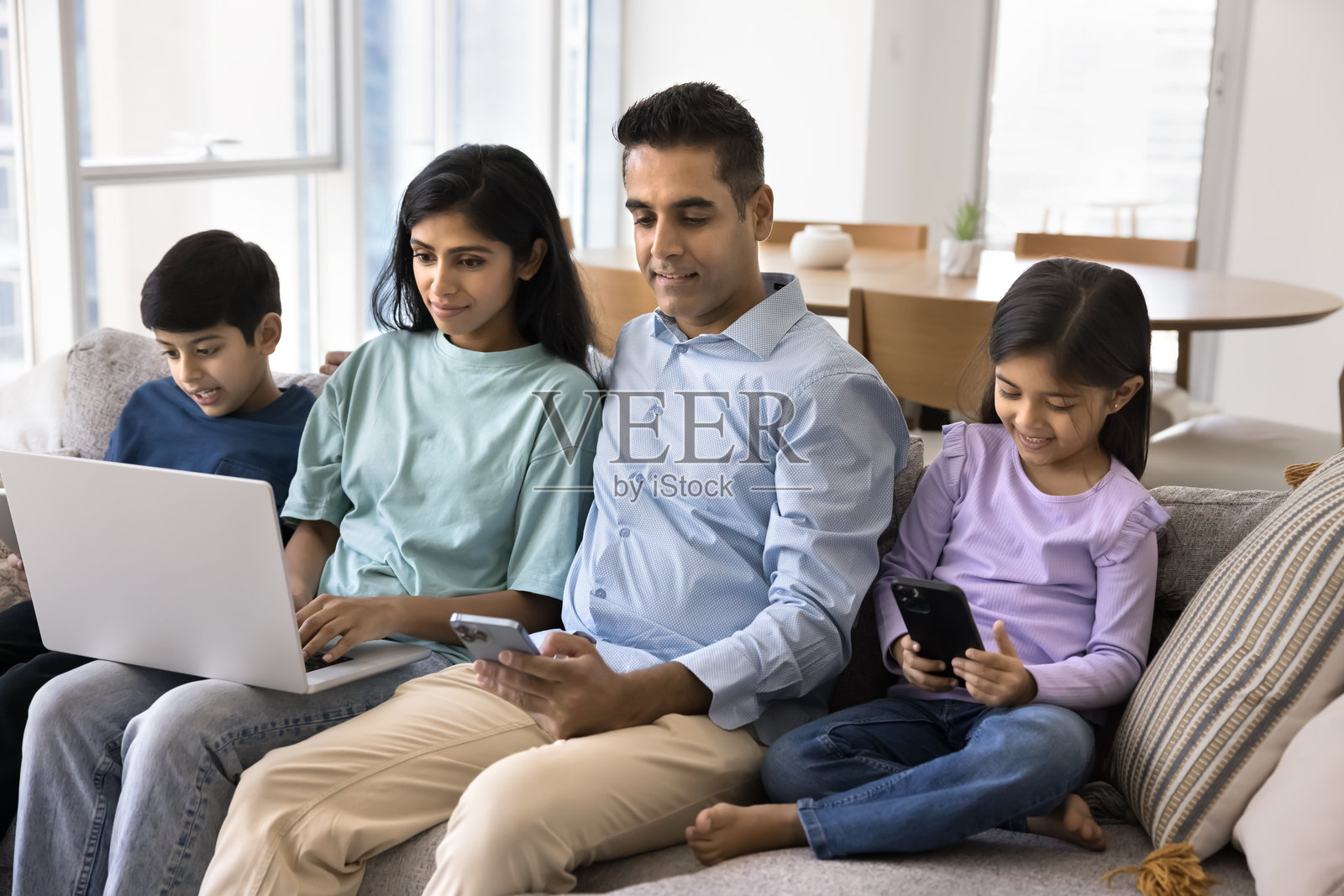 一对印度父母和两个专注于电子设备的孩子照片摄影图片