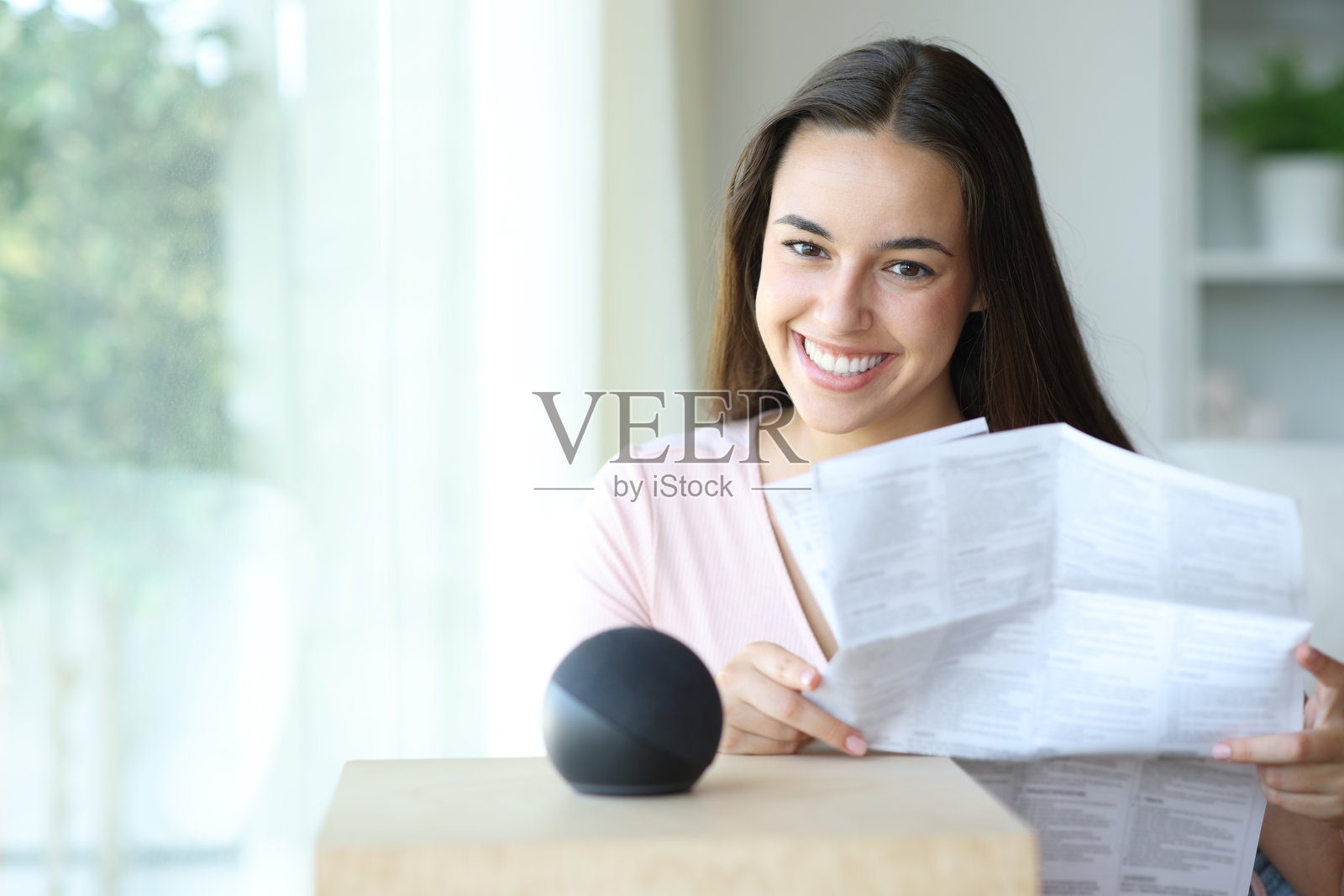 快乐的女人手持智能音箱手册,正看着你。照片摄影图片