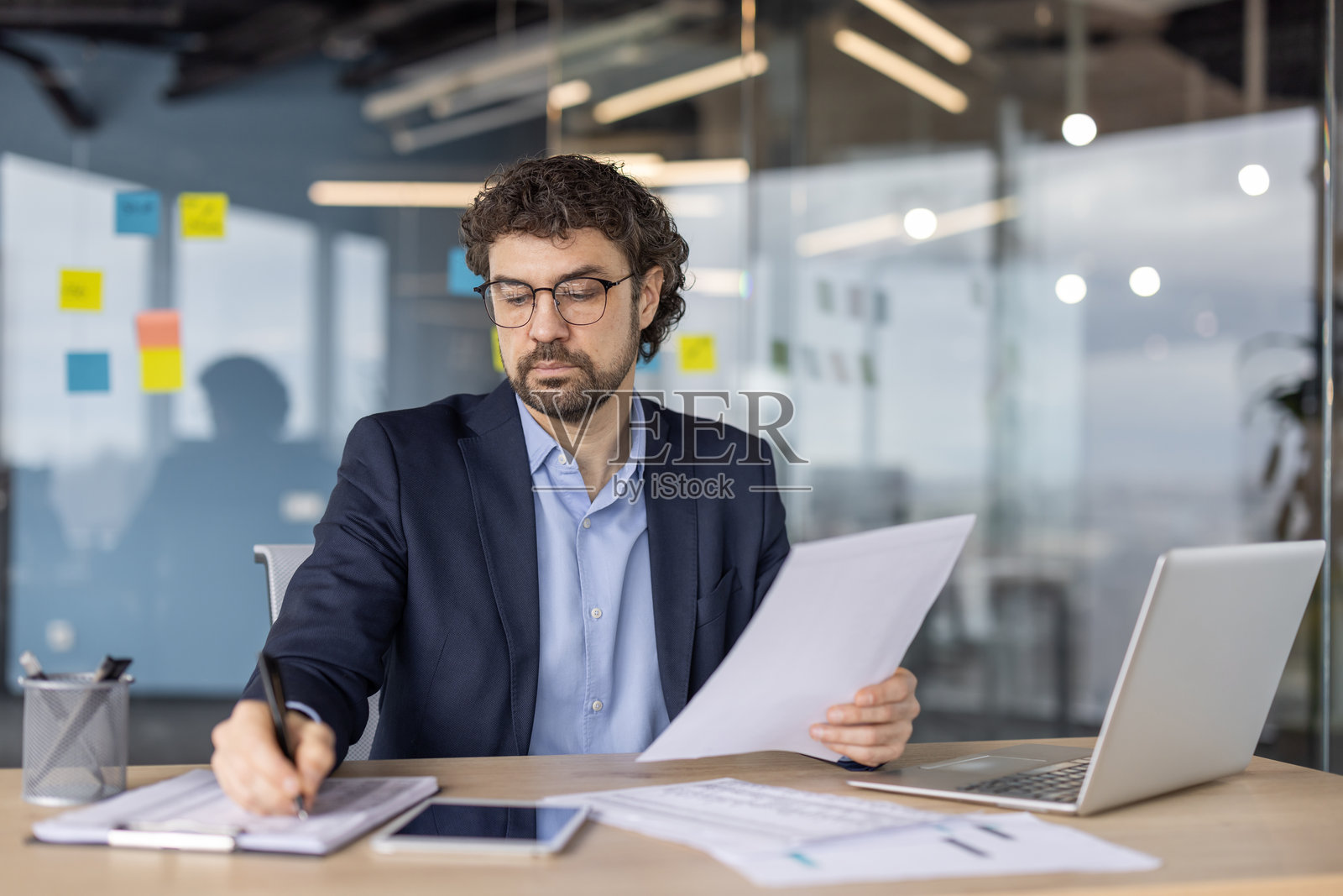 成熟的金融专家在现代办公室内专注而精准地使用笔记本电脑和智能手机审阅文件。照片摄影图片