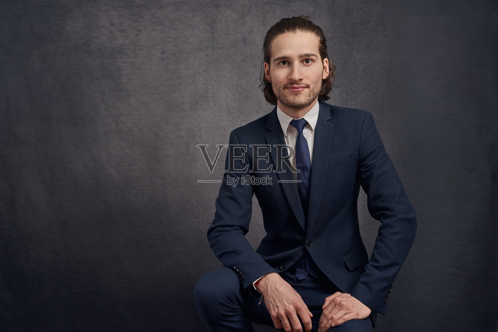 穿着西装的年轻男子坐在灰色背景前的肖像照片摄影图片