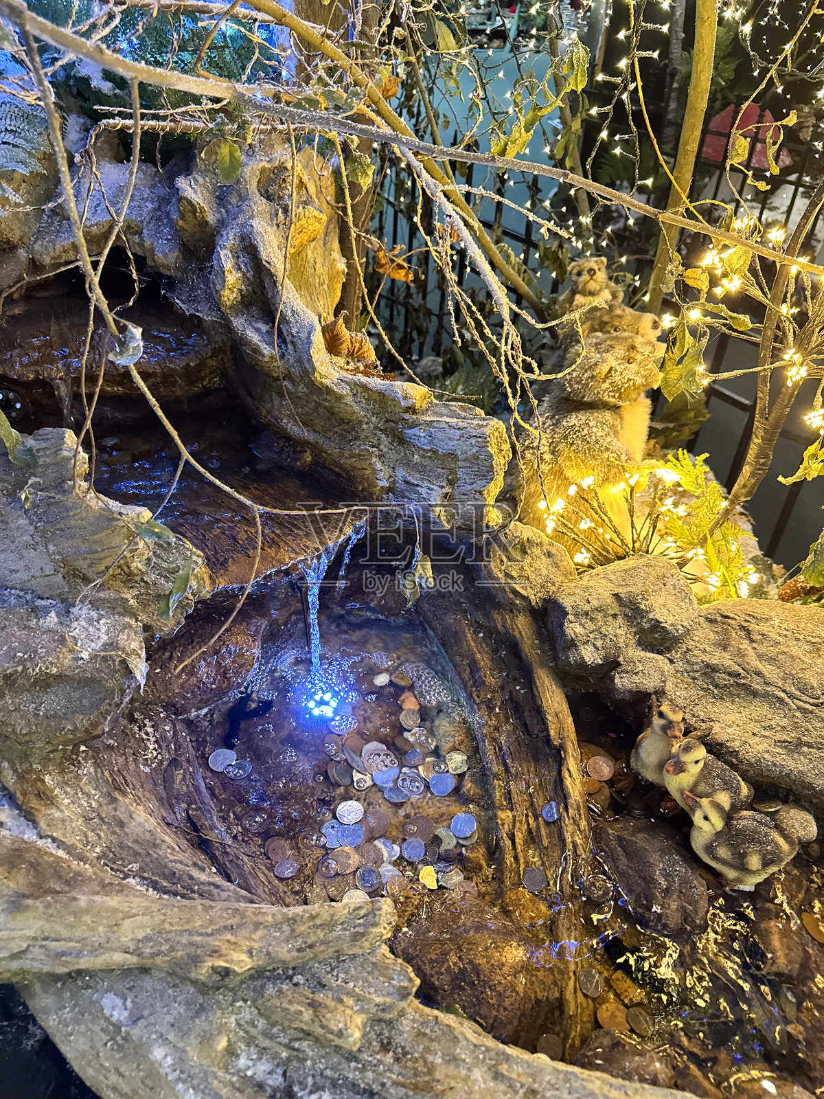 圣诞冬季展示的特写图像,瀑布池,流动的水,三只小鸭子和森林生物的雕像,许愿井里的硬币,点亮的仙女灯,俯视图,聚焦于前景照片摄影图片