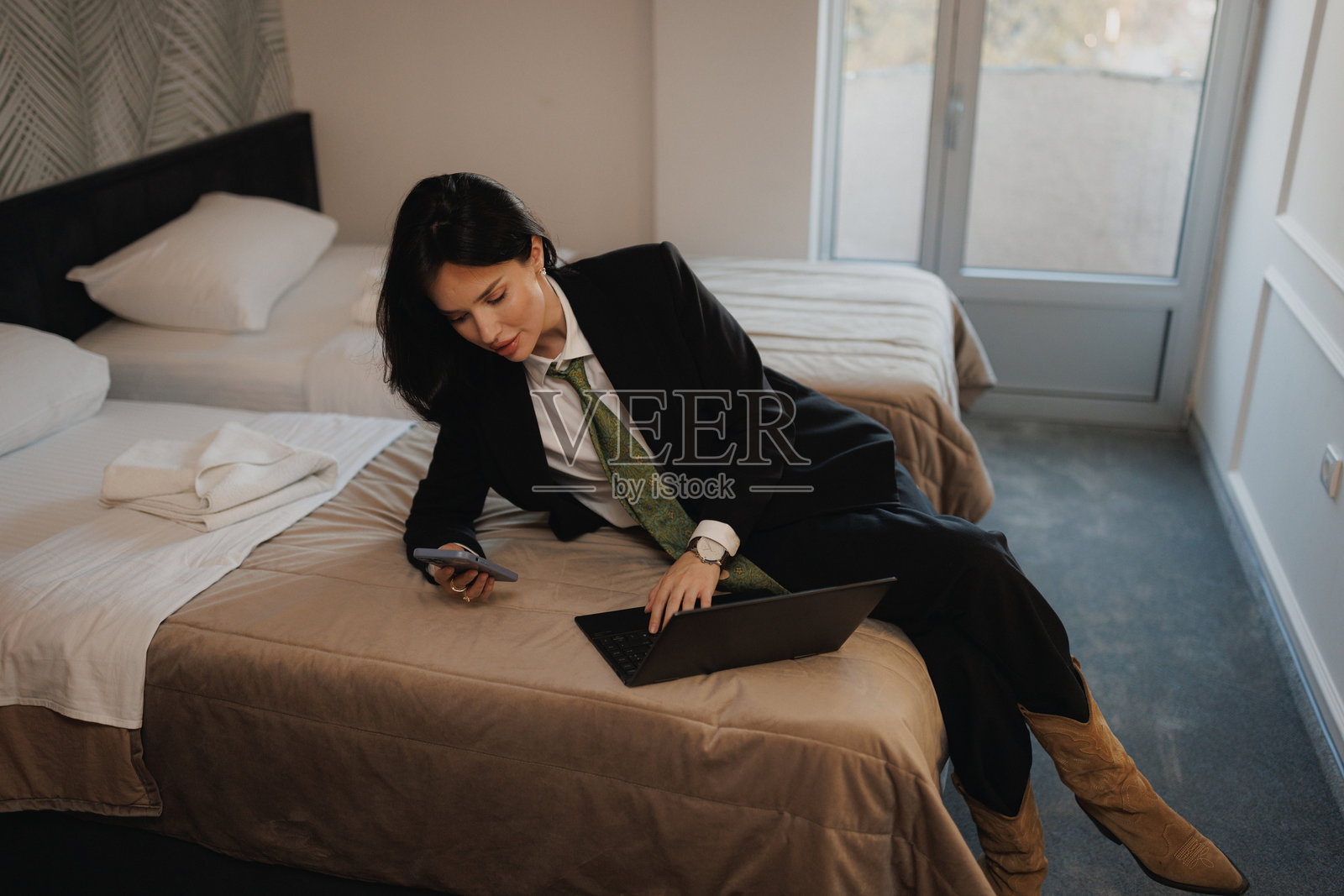 时尚年轻女企业家在酒店房间管理她的笔记本电脑和商务电话 - 投资者和金融专家照片摄影图片