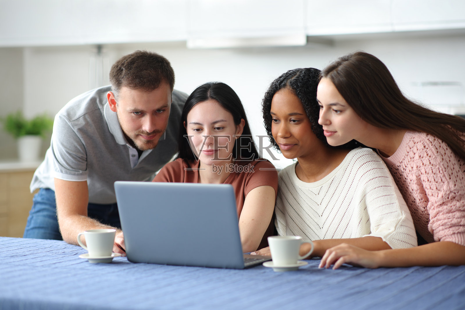 四个严肃的跨种族朋友在厨房里使用笔记本电脑照片摄影图片