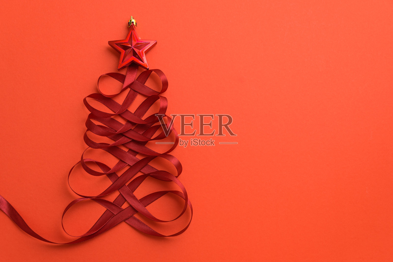 红色背景上用红色丝带和星形玩具制作的圣诞树。俯视图。平铺展示。照片摄影图片