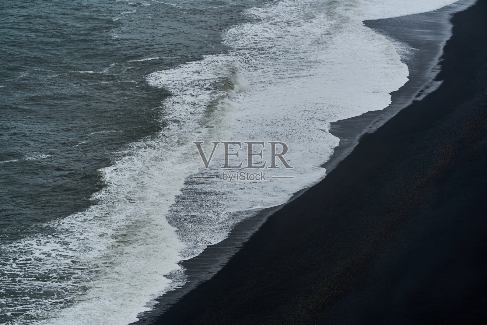 海浪拍打在黑沙滩上,形成白色泡沫照片摄影图片