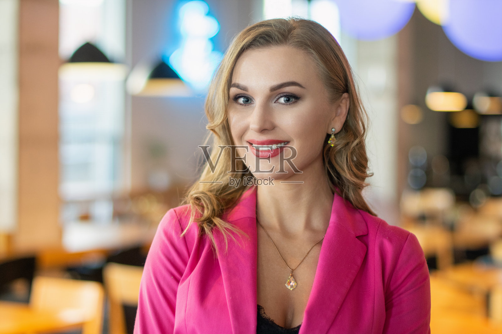 微笑的女商人穿着粉色西装在餐厅摆姿势照片摄影图片