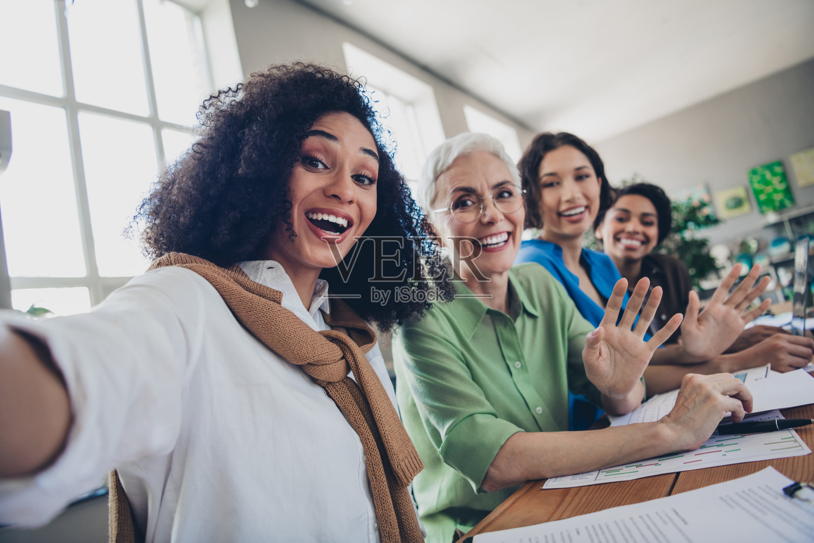 四位多元化女性商界领袖和女权主义者在现代办公室内自拍并挥手致意照片摄影图片