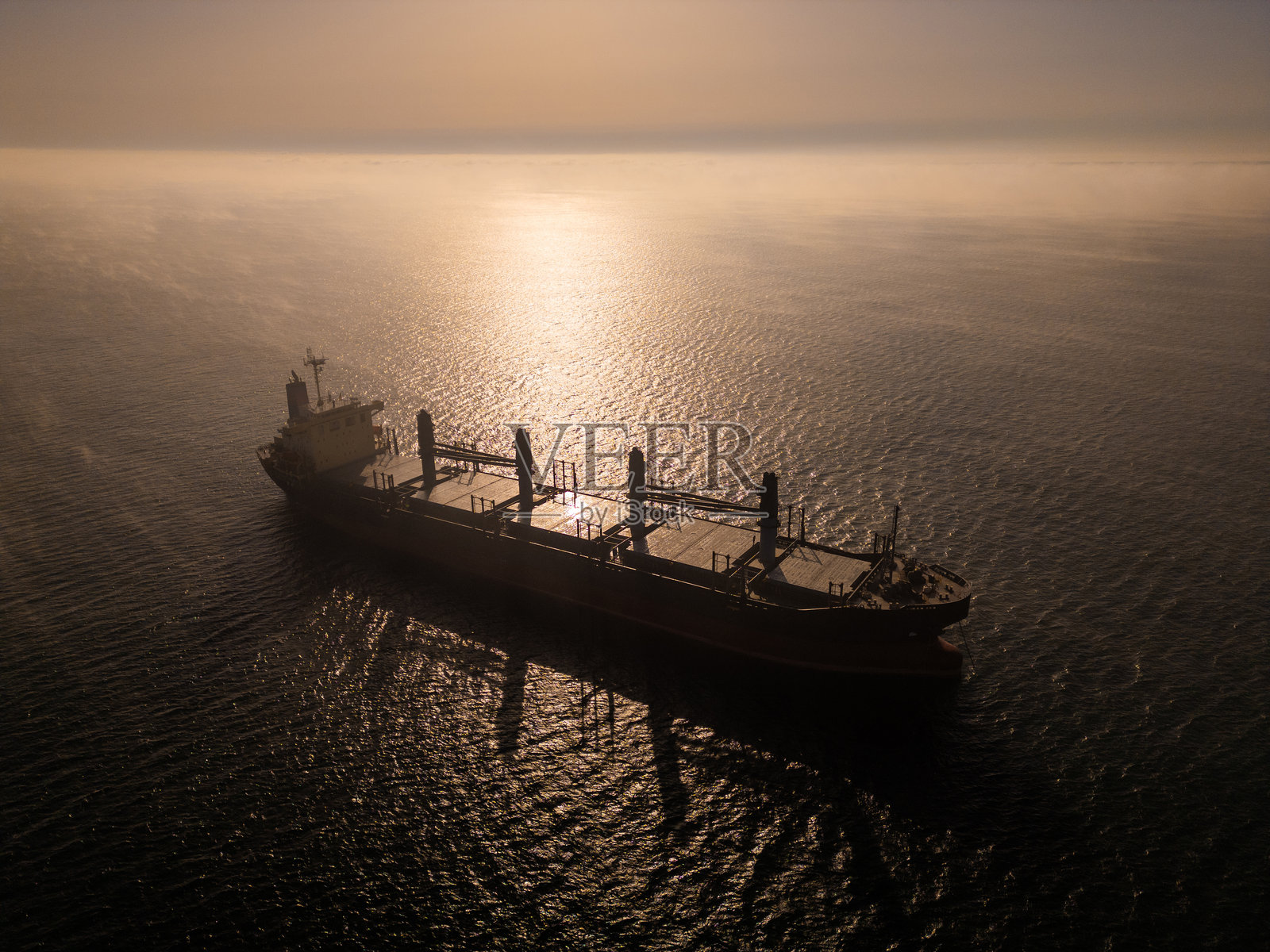 航拍无人机镜头捕捉到一艘货船在雾气弥漫的水面上航行,阳光的倒影营造出宁静而神秘的海洋场景,非常适合工业和航海主题。照片摄影图片