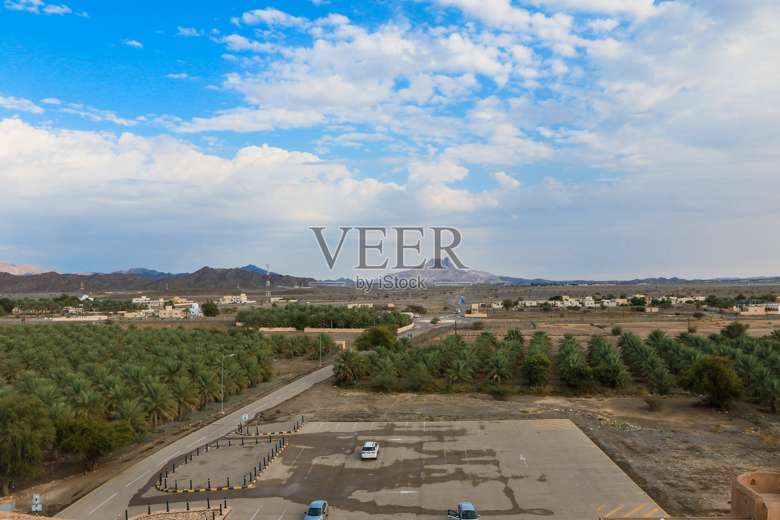 阿曼在晴朗白天下郁郁葱葱的棕榈树林和崎岖山脉的全景视图照片摄影图片