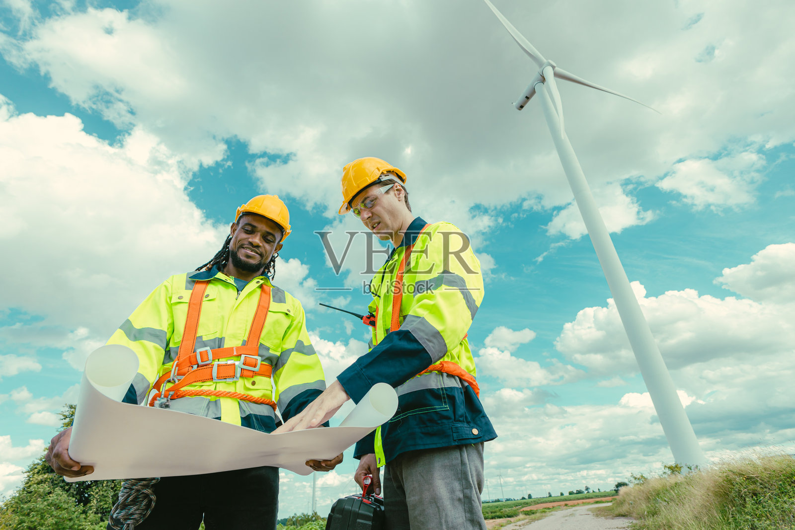 工程师团队由黑白男性工人组成,在风电场的风力发电机农场户外进行测量工作,手持平面图。照片摄影图片