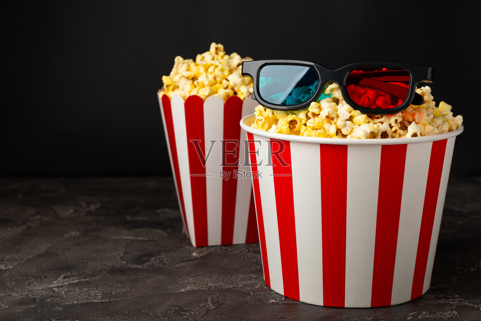 美味的爆米花装在桶里,旁边是冰凉的可乐饮料,还有电影票、电影拍板和3D眼镜,背景色彩鲜艳。电影院概念。观看电影。留白处。照片摄影图片