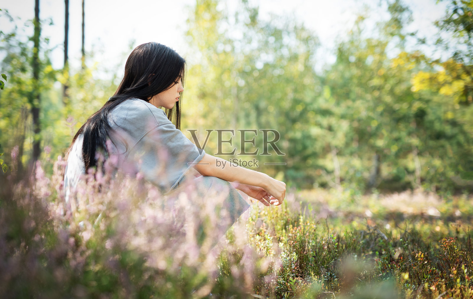 一位女性安静地坐在阳光明媚的下午,周围被野花环绕的宁静森林空地上。照片摄影图片