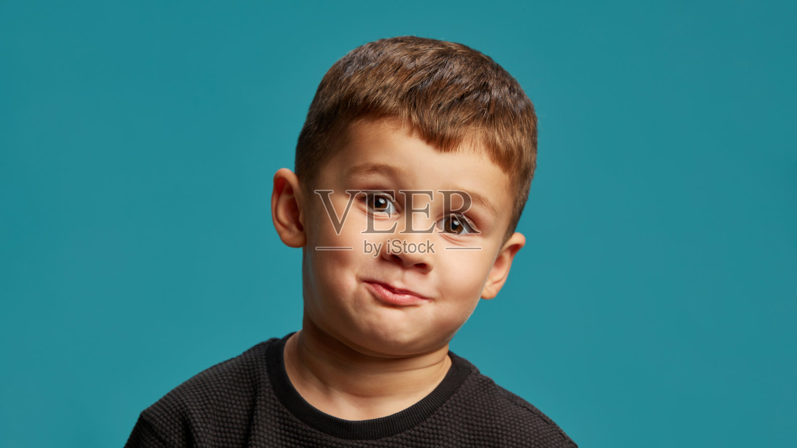 小男孩做出顽皮的表情,嘴唇嘟起,展现出滑稽和调皮的气息,背景为蓝色摄影棚。照片摄影图片