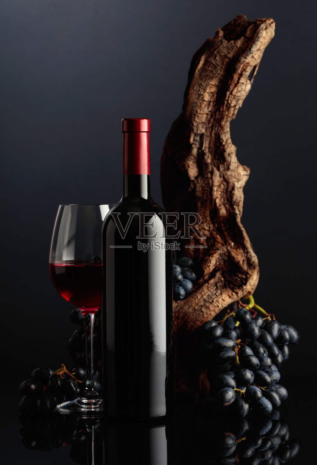 一瓶红酒和一杯红酒,旁边有一根老树桩和蓝色葡萄。照片摄影图片