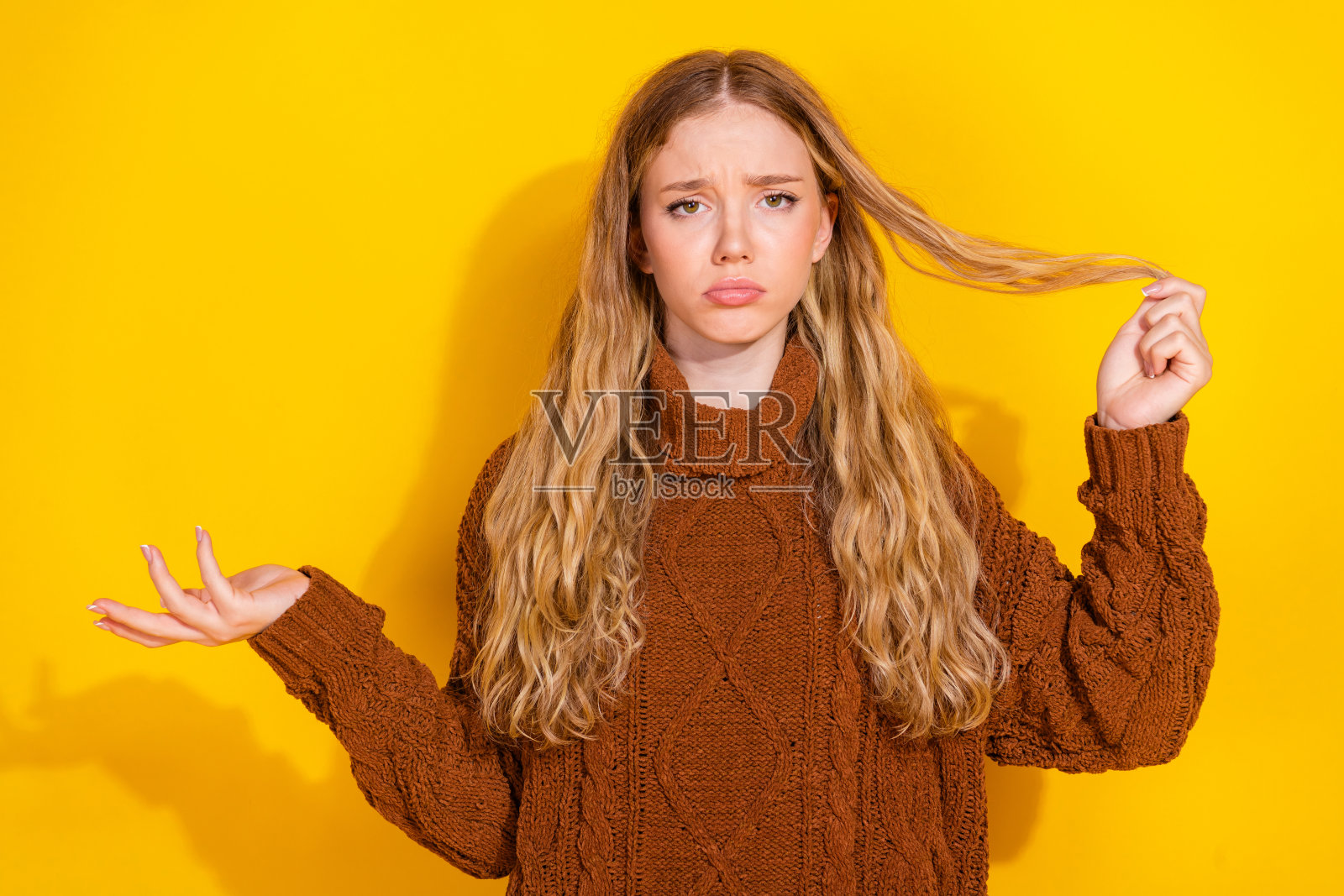 年轻女孩的肖像,面带愁苦,触摸受损的头发,穿着毛衣,背景为黄色。照片摄影图片