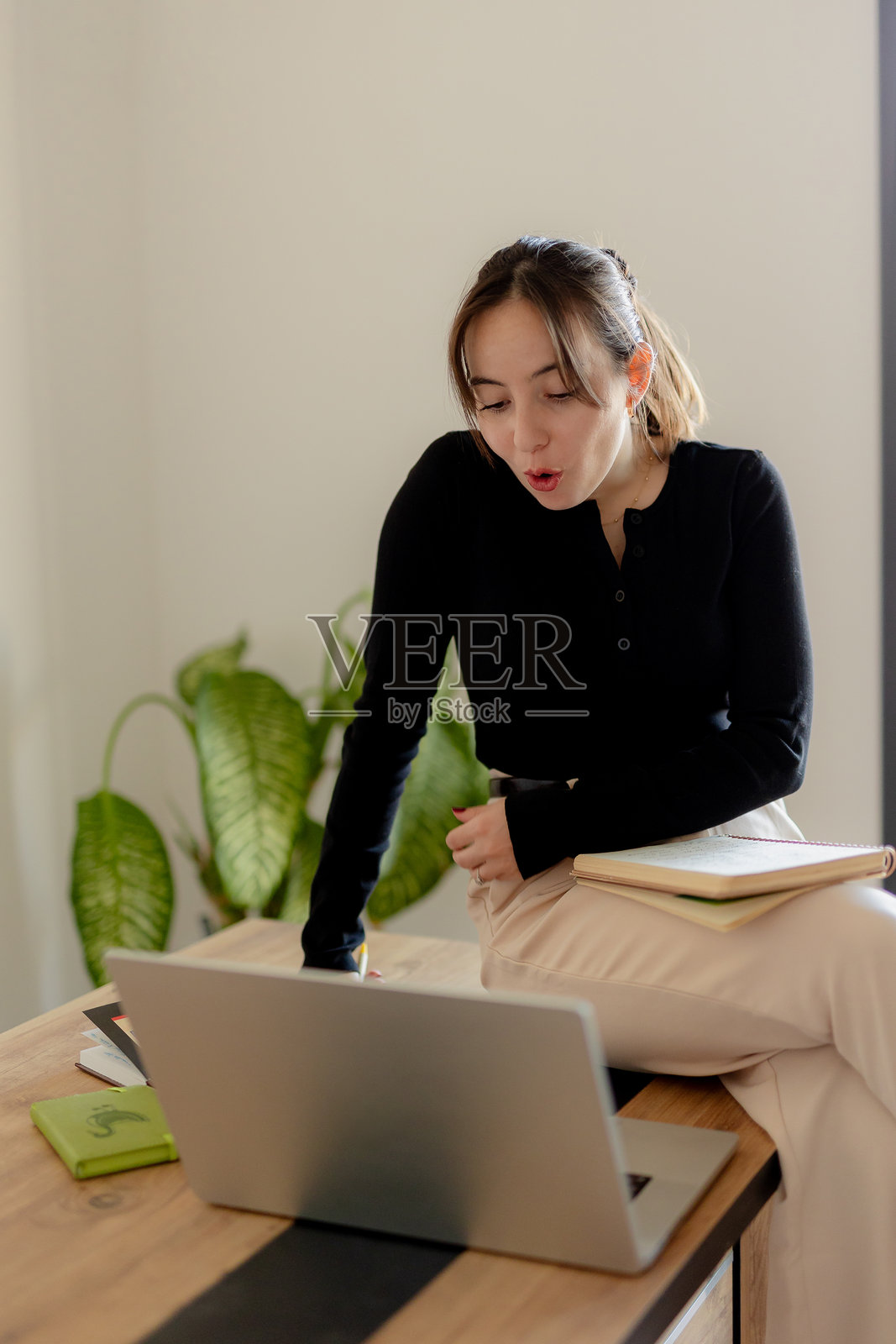 自信的年轻女商人在现代办公室环境中庆祝成功,手边有笔记本电脑和文件。照片摄影图片