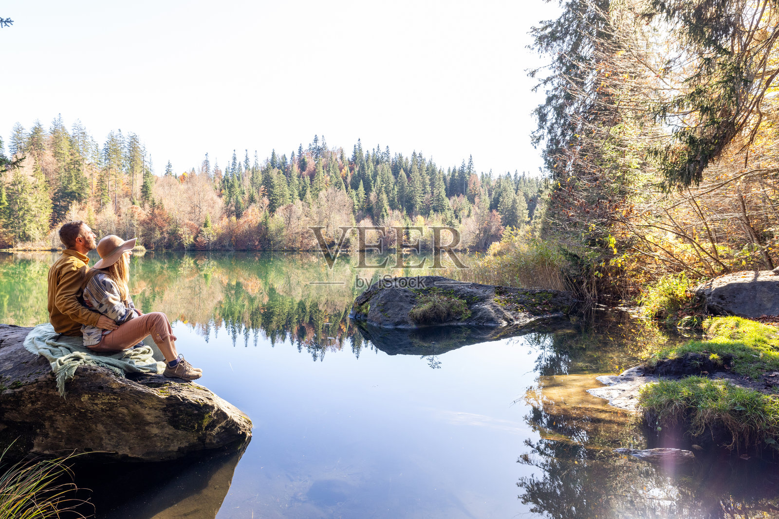 秋季森林中,情侣在湖边岩石上放松照片摄影图片