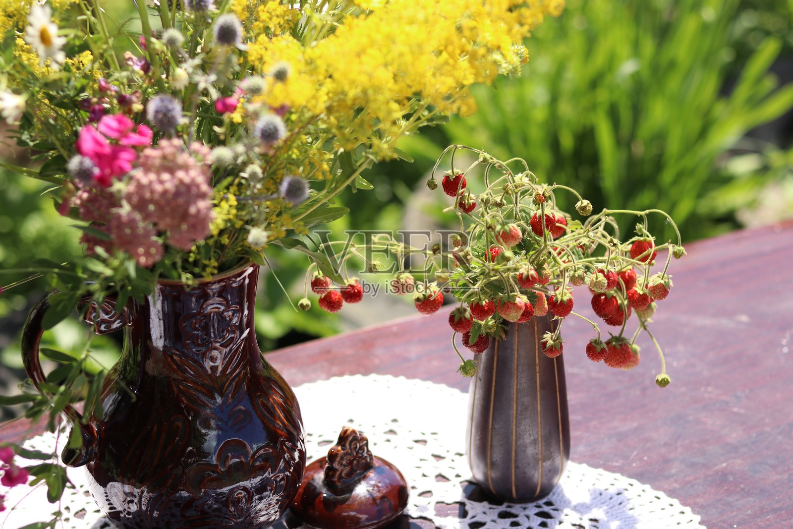 花园桌子上的陶土花瓶,里面插着野花,旁边还有一个装有草莓的花瓶照片摄影图片