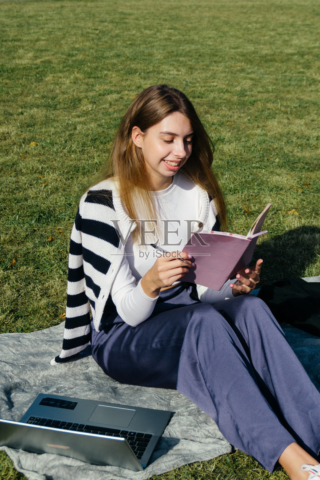 大学校园的女学生在夏季假期的绿草地上使用笔记本电脑学习并做笔记。照片摄影图片