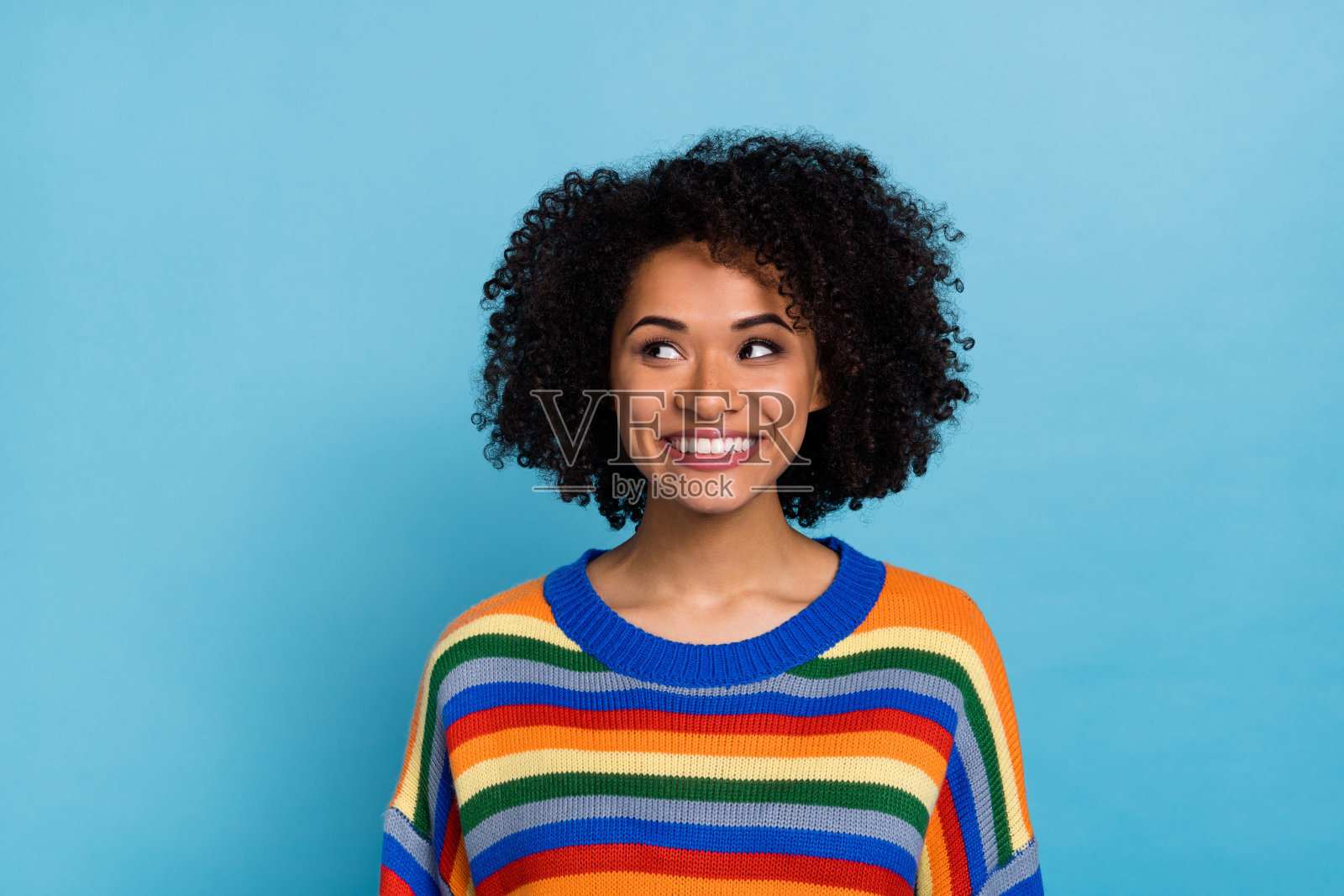 穿着彩色毛衣的女士,留着令人印象深刻的波浪发型,背景为蓝色。照片摄影图片