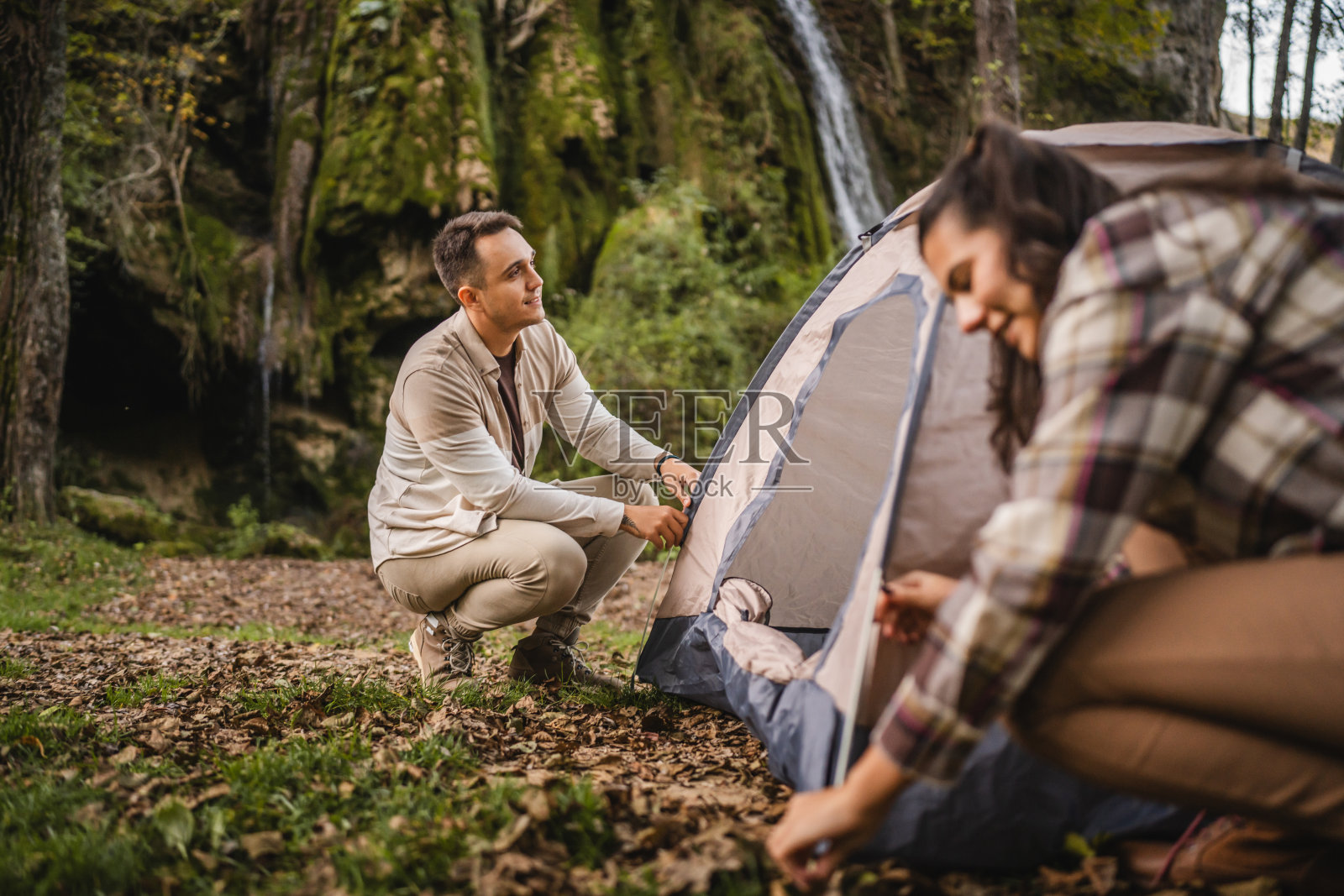 一对徒步旅行者在森林中的瀑布前一起搭帐篷照片摄影图片