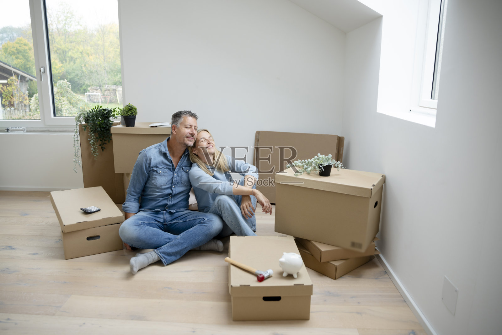 中年夫妇坐在新公寓的地板上,周围是搬家箱子。照片摄影图片