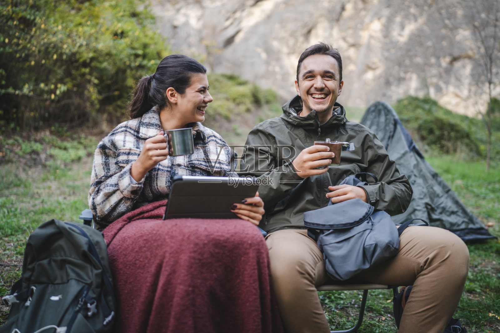 男朋友和女朋友露营者坐在帐篷前,享受饮料。照片摄影图片